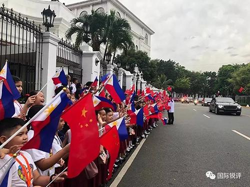 20日，來自馬尼拉當地三所小學的千名小學生站在總統府道路兩側揮舞兩國國旗，歡迎習主席車隊。（圖片來源：中央廣播電視總臺央視新聞 記者鄧雪梅拍攝）